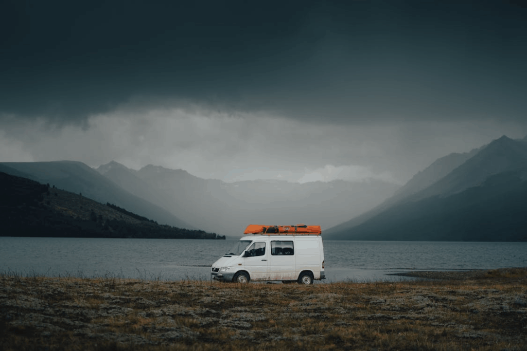 White camper van parked by a lake with mountains in the background during a cloudy day, a perfect long weekend getaway scene.