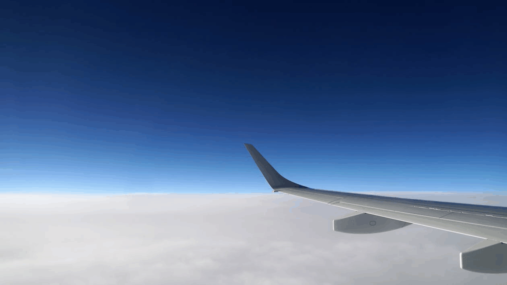 View from airplane window showing wing above the clouds during flight under a clear blue sky, perfect visual for air travel