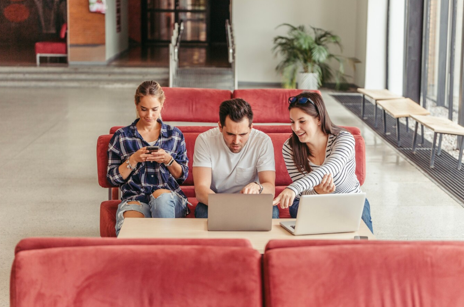 Digital nomads working on laptops in a modern coworking lounge with casual seating and natural light