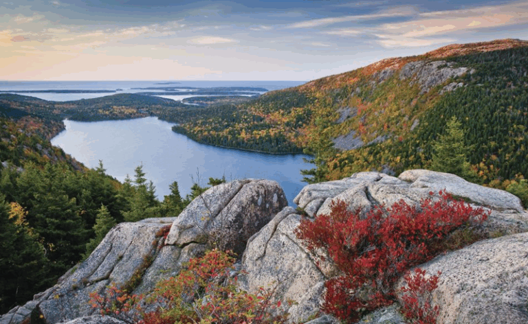 Scenic overlook of Jordan Pond and fall foliage in Acadia National Park, featuring rocky cliffs and colorful trees.