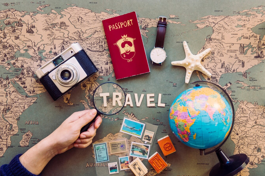 Flat lay of international travel essentials on world map including passport, vintage camera, globe, travel stamps, and watch.