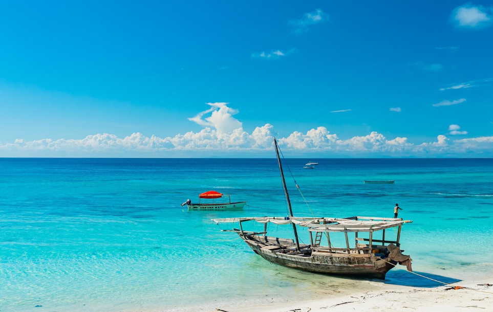 Traditional dhow boat on a white sand beach in Zanzibar, Tanzania, with turquoise Indian Ocean water and clear blue skies
