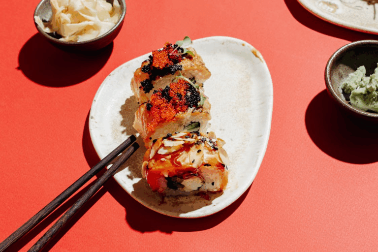 Assorted sushi rolls topped with fish roe and sauce on a ceramic plate with chopsticks