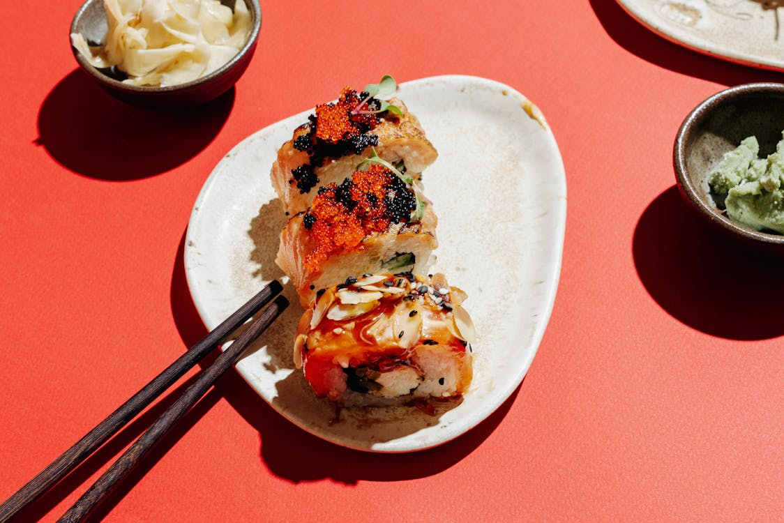 Assorted sushi rolls topped with fish roe and sauce on a ceramic plate with chopsticks