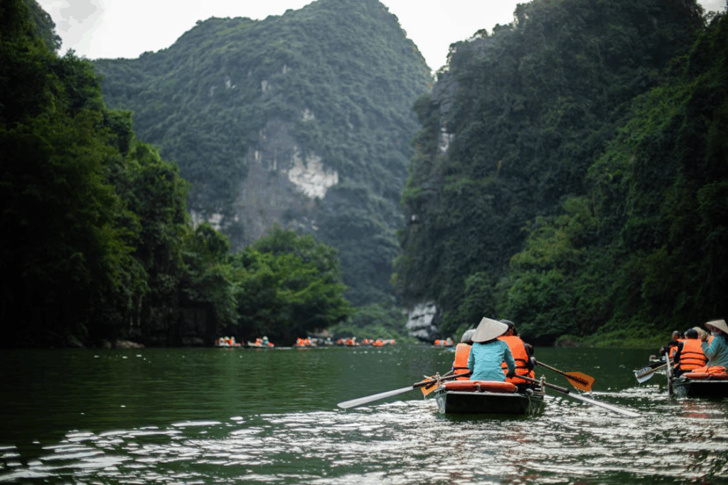 Tourists paddling through lush limestone cliffs in Ninh Binh, Vietnam, during a Trang An boat tour
