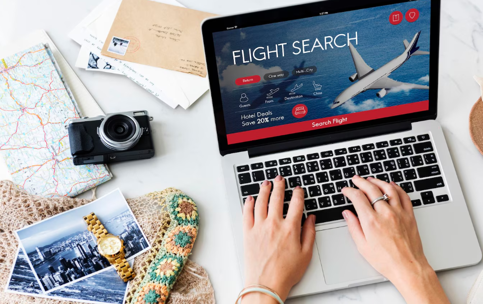 Searching for last-minute travel deals on a flight booking website with travel essentials on desk