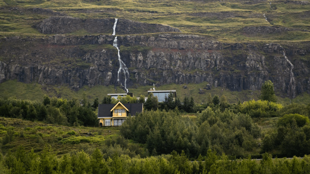 Cozy off-the-grid destination surrounded by forest with a cascading waterfall on a rocky cliff in the background.