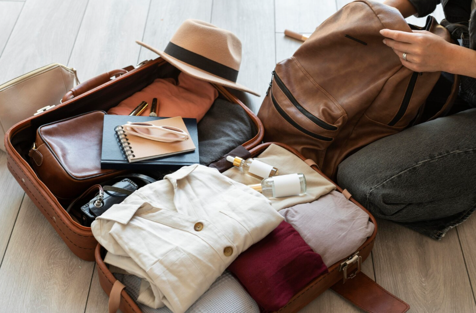 Open carry-on suitcase and leather backpack with capsule wardrobe, toiletries, and travel essentials for a long trip.