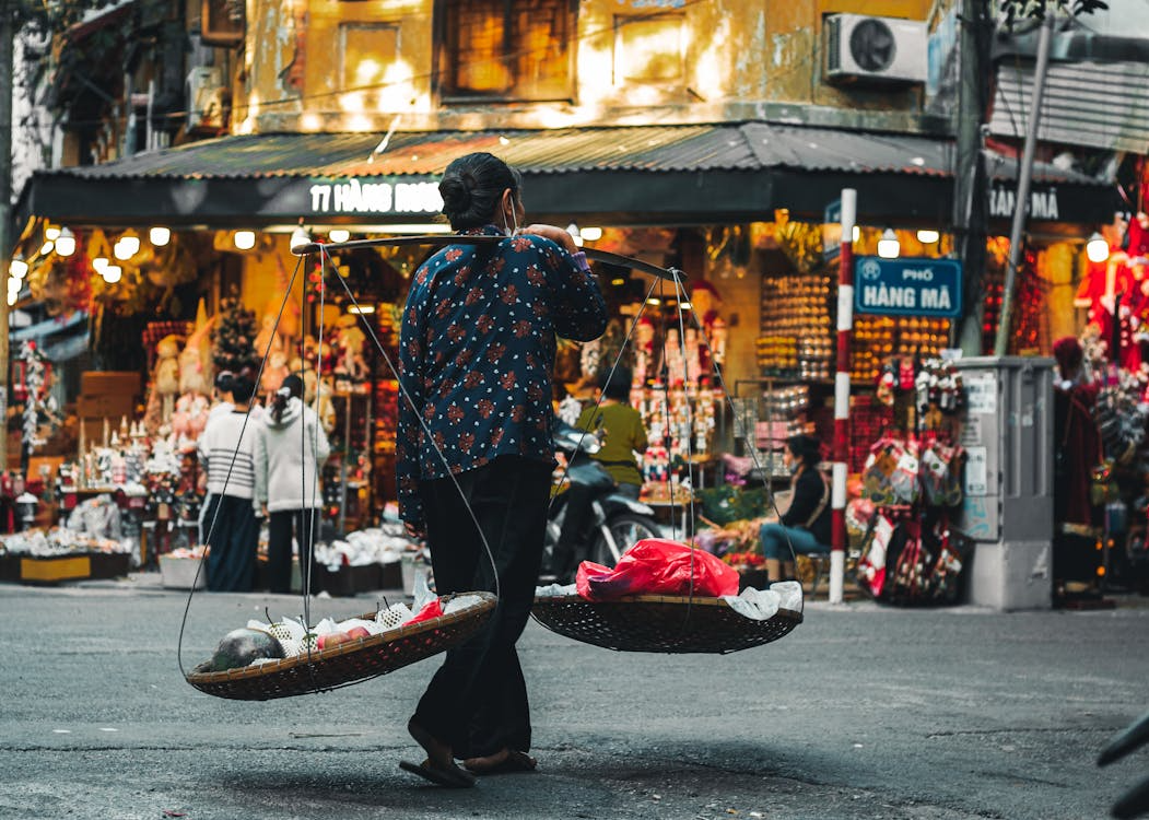 Street vendor carrying traditional baskets in Hanoi’s Old Quarter, highlighting Vietnam as a cheap country to visit