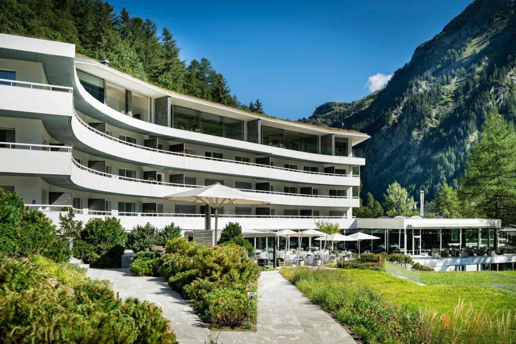 white concrete building near green trees and mountain during daytime